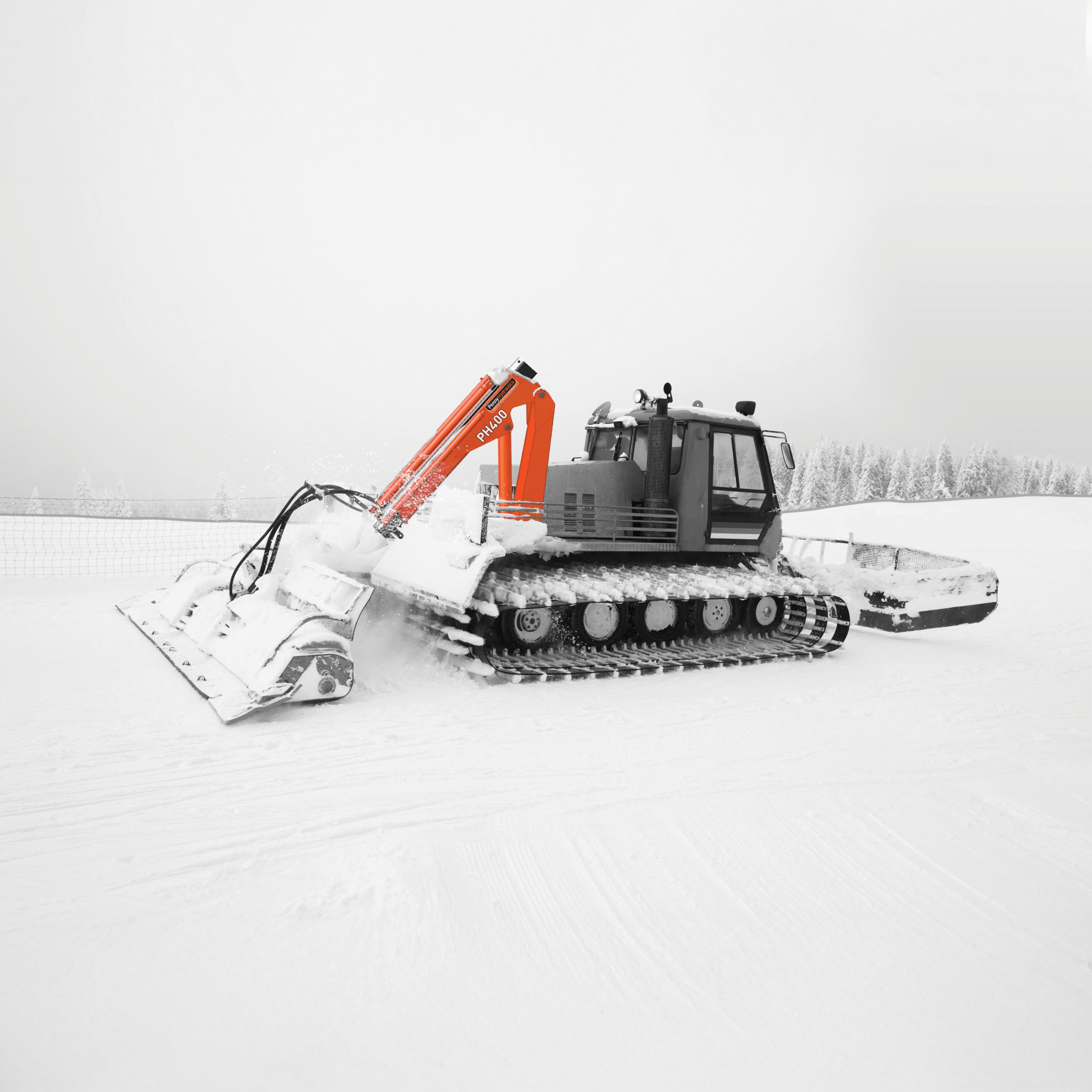A snowcat vehicle with orange machinery arms clears snow on a wintry landscape. The ground and distant trees are covered in snow, and the sky is overcast, creating a monochrome winter scene.