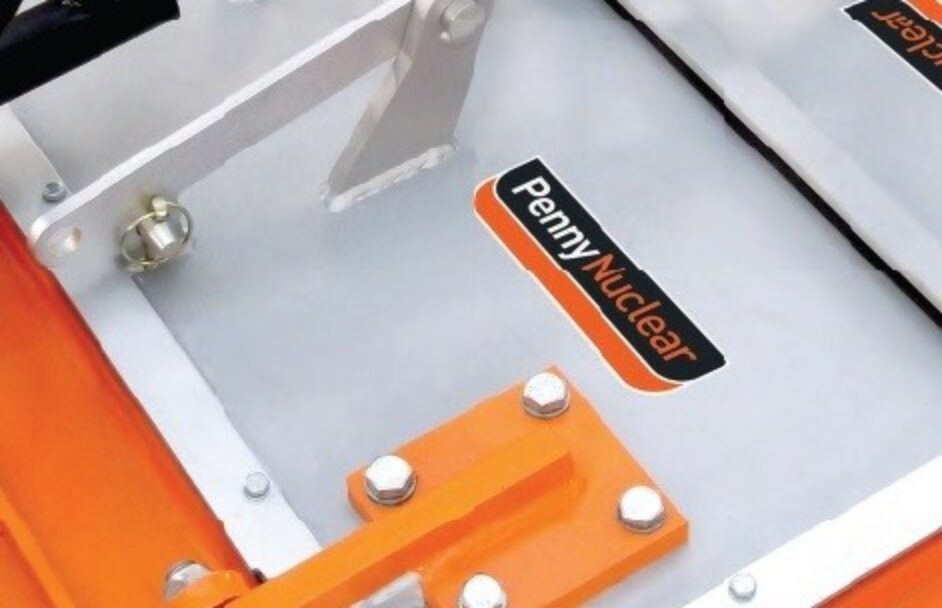 Close-up of metallic equipment with bolts and an orange base, displaying a black and orange label that reads Penny Nuclear.